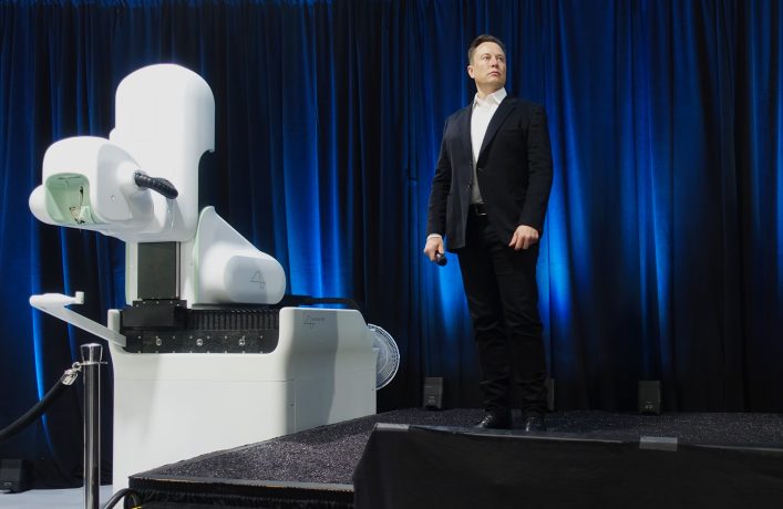 Elon Musk standing next to futuristic white device on stage